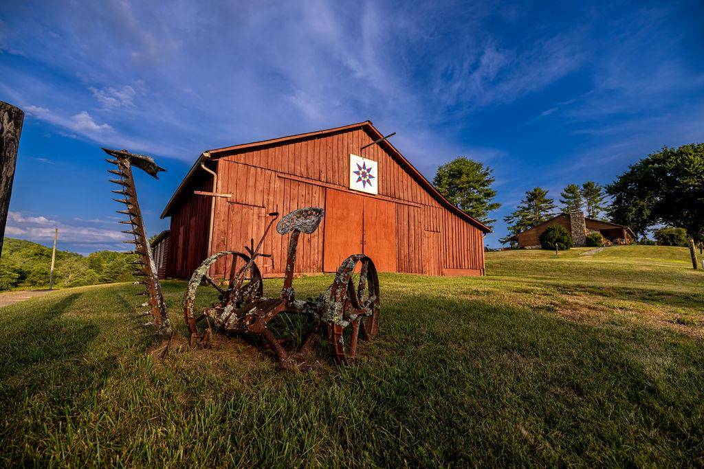 A red barn with a quilt square and an old horse-drawn implement on the lawn.