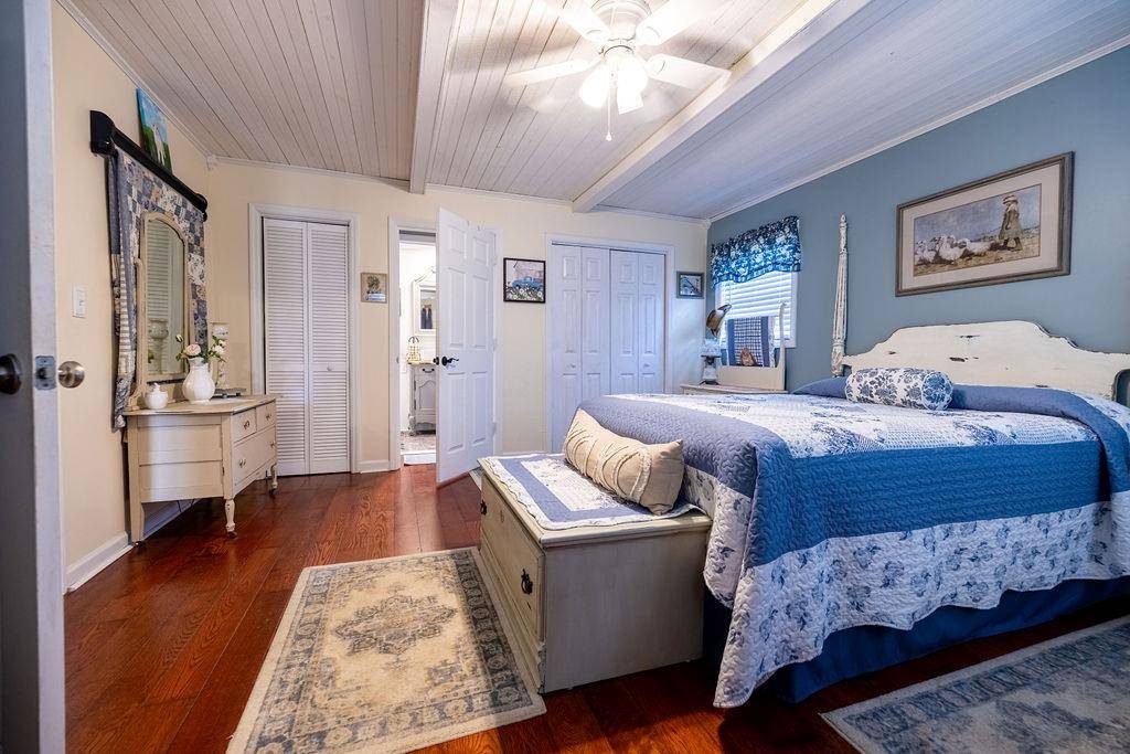 An inn bedroom with a blue quilt, white dresser and hardwood floor.